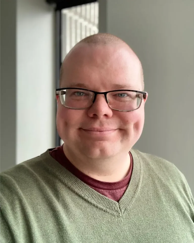 Freddie Wyatt, therapist at SEC LLC, smiling at the camera wearing rectangular thin framed glasses and an olive green shirt.