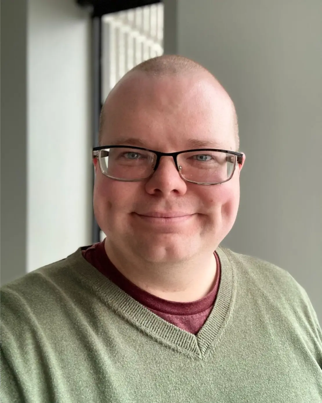 Freddie Wyatt, therapist at SEC LLC, smiling at the camera wearing rectangular thin framed glasses and an olive green shirt.